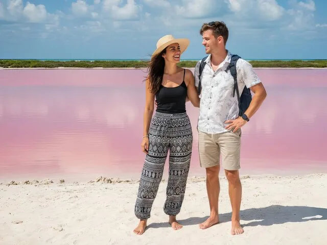 Una coppia sorridente in piedi su una spiaggia di sabbia bianca vicino a un'acqua rosa brillante.