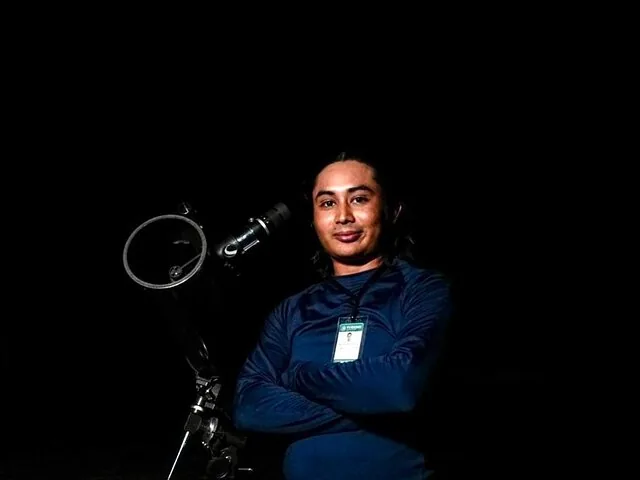 Una persona è in piedi accanto a un telescopio di notte.
