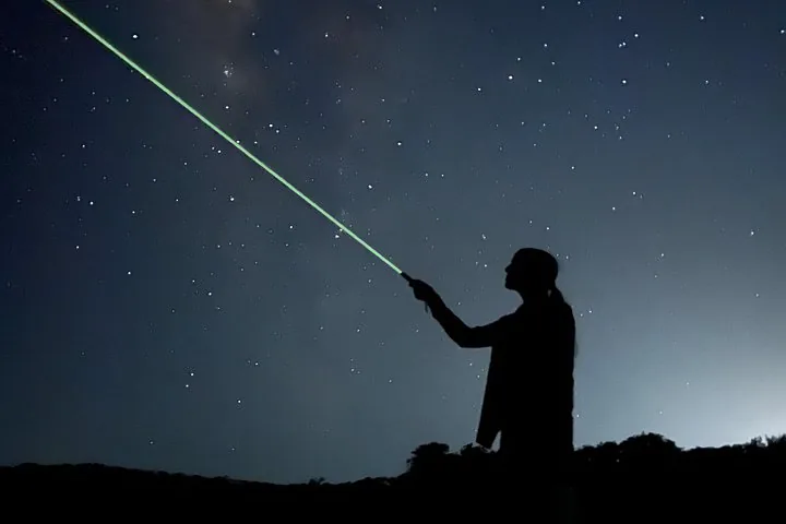 Silhouette einer Person, die einen Laser in den sternklaren Nachthimmel richtet.