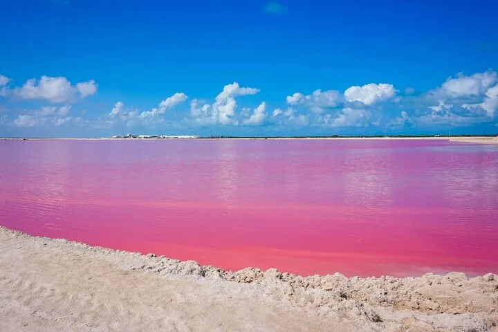 Bright pink water in a salt lagoon under a blue sky.