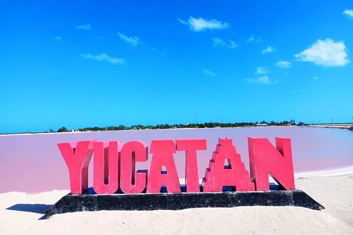 Large red YUCATAN sign on the shore of a pink salt lake.